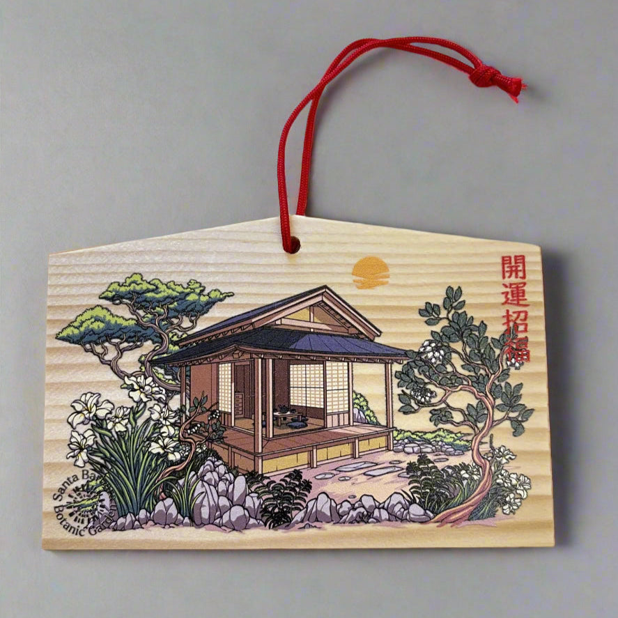 Wooden ornament with Japanese house illustration and red string on a textured white background
